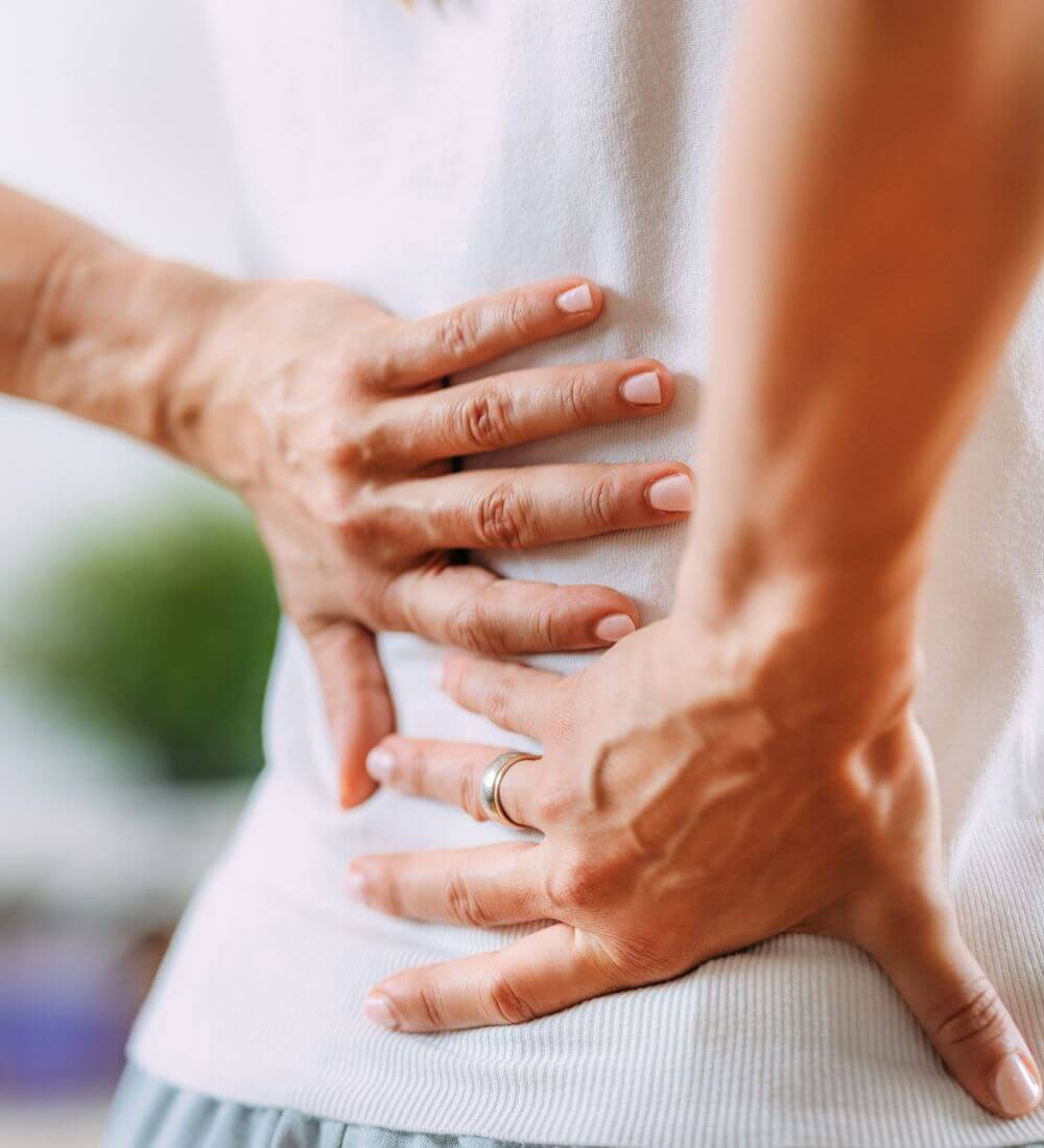 A person is holding their lower back with both hands, indicating discomfort or pain.