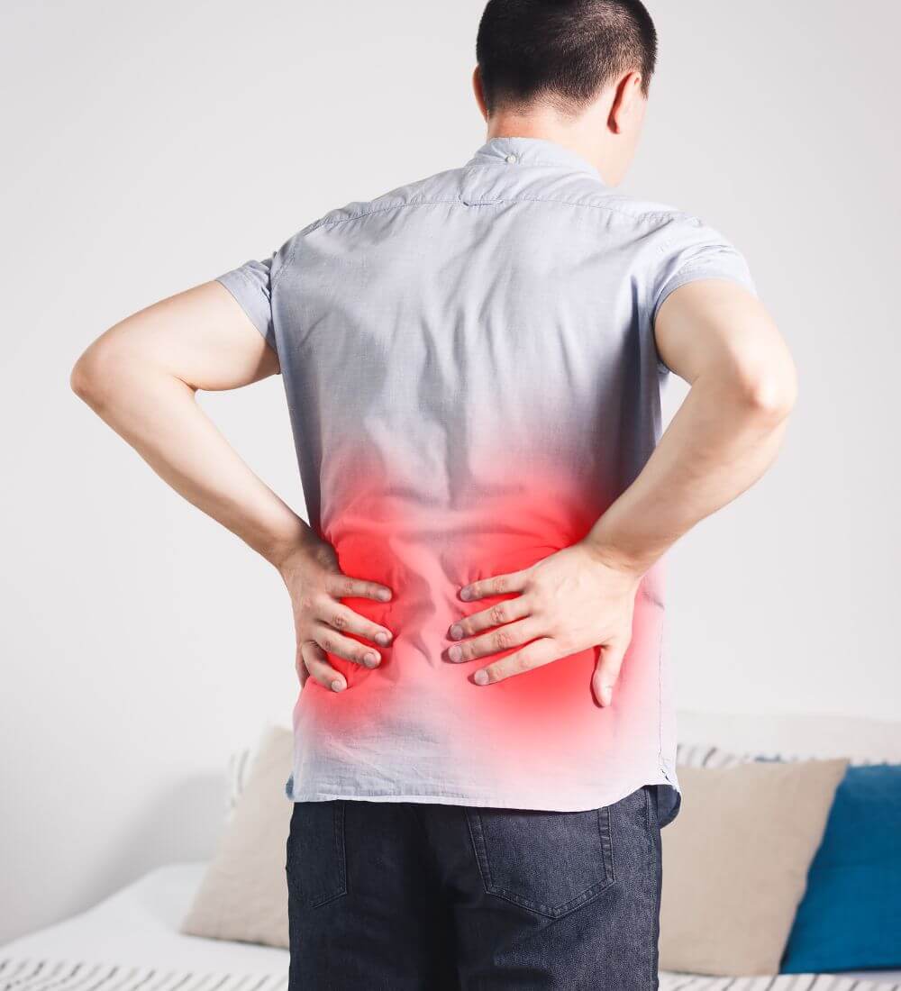 A man standing with his back to the camera, holding his lower back where there is a red highlight, indicating pain.